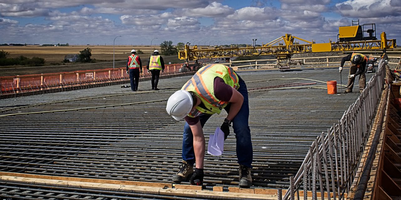 A bridge engineer inspecting spacing diameter and height of steel reinforcing bars with a tape measure on the bridge deck prior to pouring concrete on the reinforced deck supported by steel girders