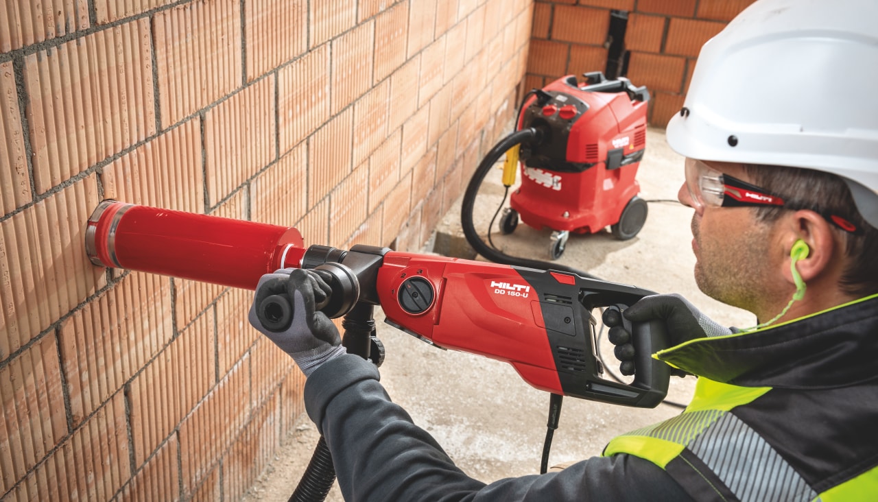 Worker performing diamond drilling in brick wall
